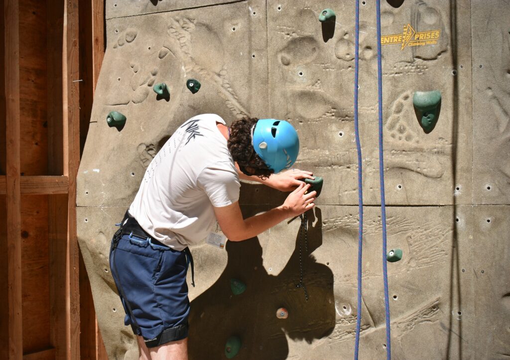 A staff member in a climbing helmet afixes a climbing hold to the climbing wall