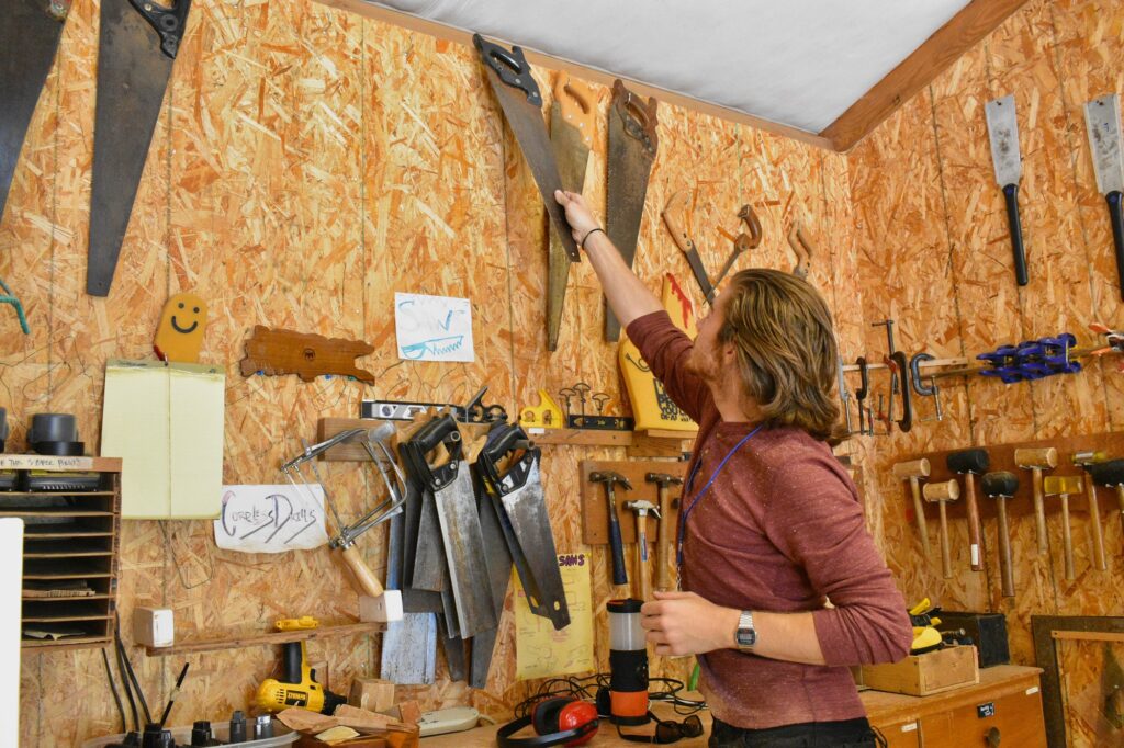A staff member hangs a metal saw on the wooden wall of the woodshop