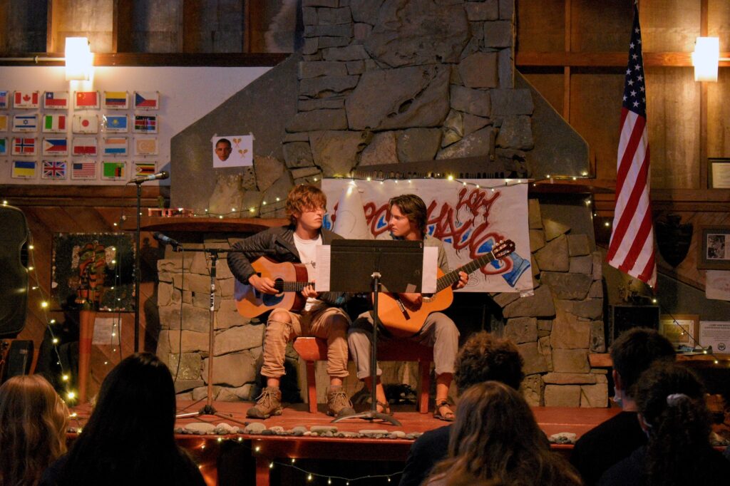 Two older campers both holding guitars perform from a lighted stage