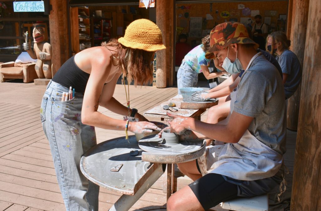 Staff member helps a camper shape clay on a pottery wheel on the craft shop porch