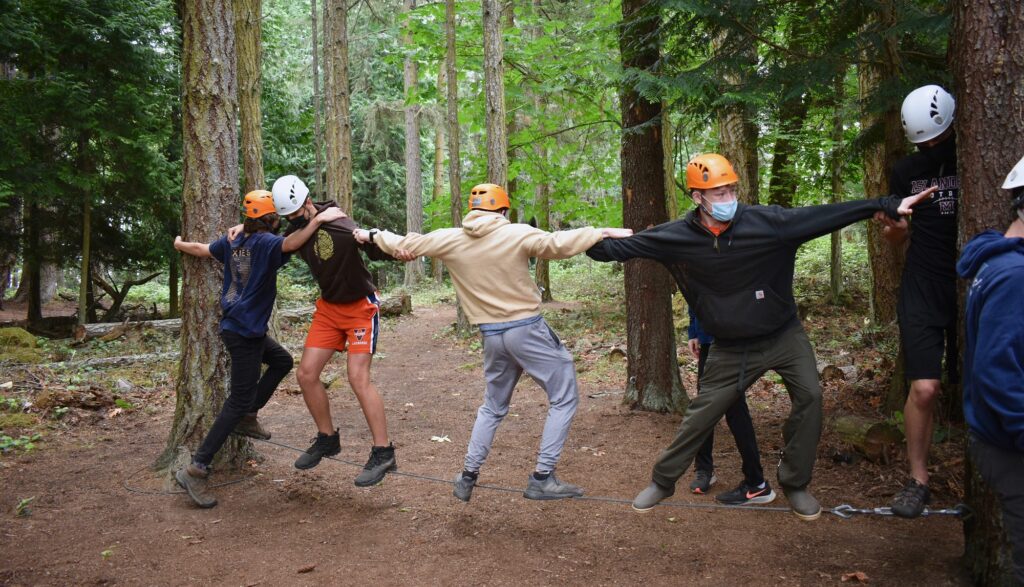 Five campers link arms as they balance on a cordsuspended above the ground at the ropes course
