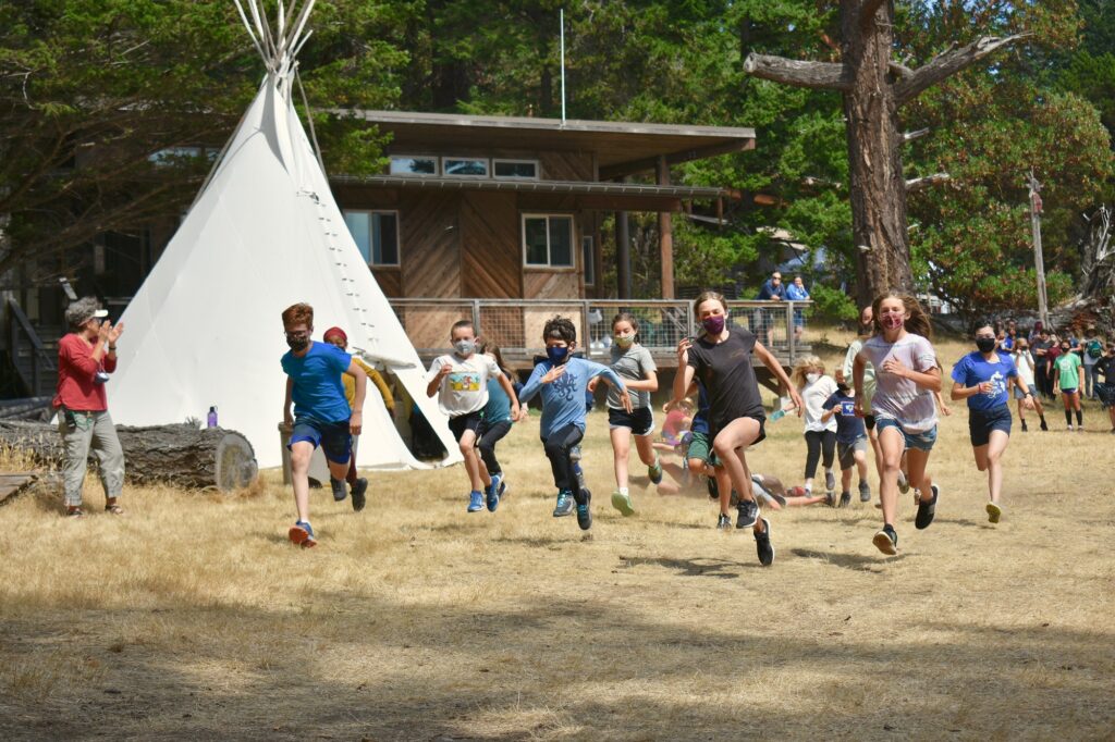 Campers run past spectators and a white tipi as they race in the fun run
