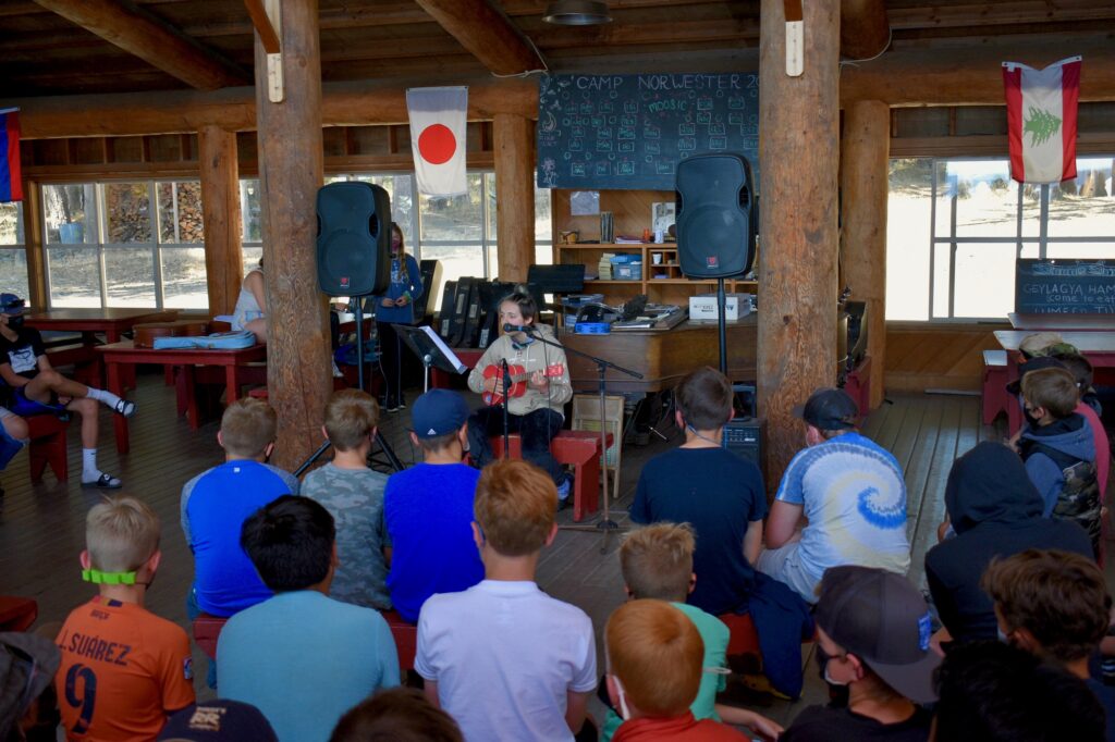 A camper plays the ukelele and sings into a microphone in front of an audience