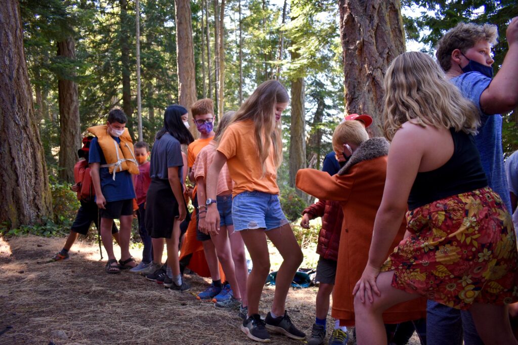 Campers dressed in orange balance on a line in the forest