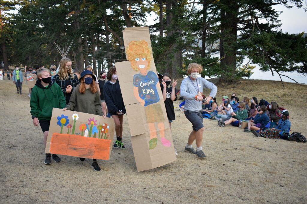 Campers and staff wearing masks carry cardboard signs in a parade line