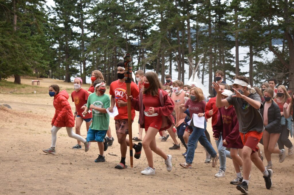 A large group of masked campers wearing red runs in formation