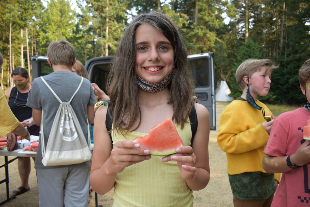 A smiling camper holds a red and green slice of watermelon