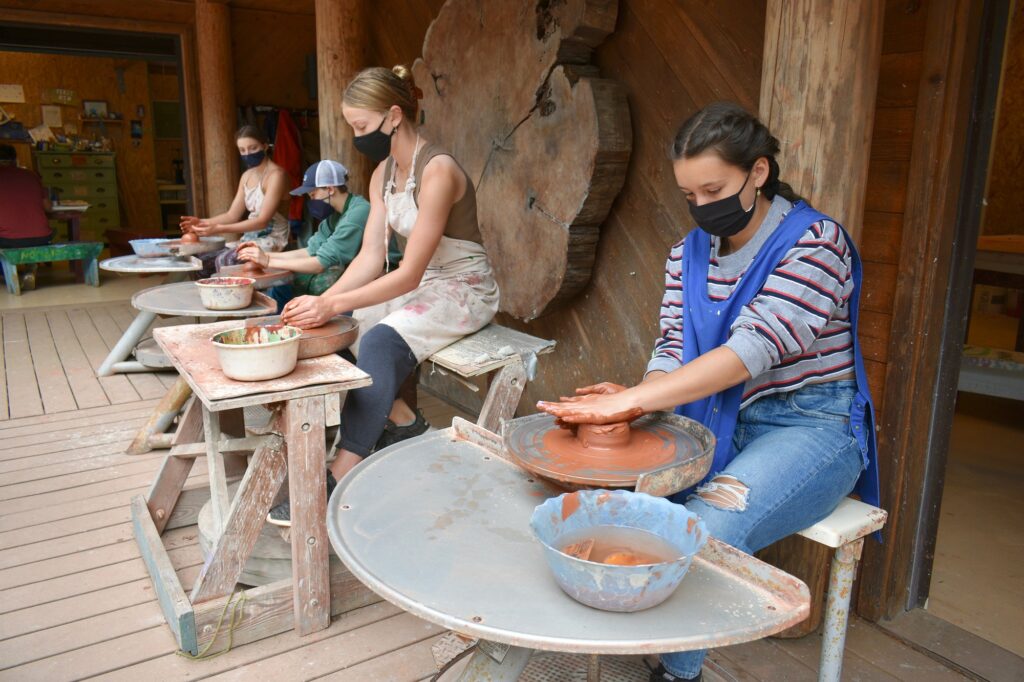 Four campers wearing masks work with clay on pottery wheels