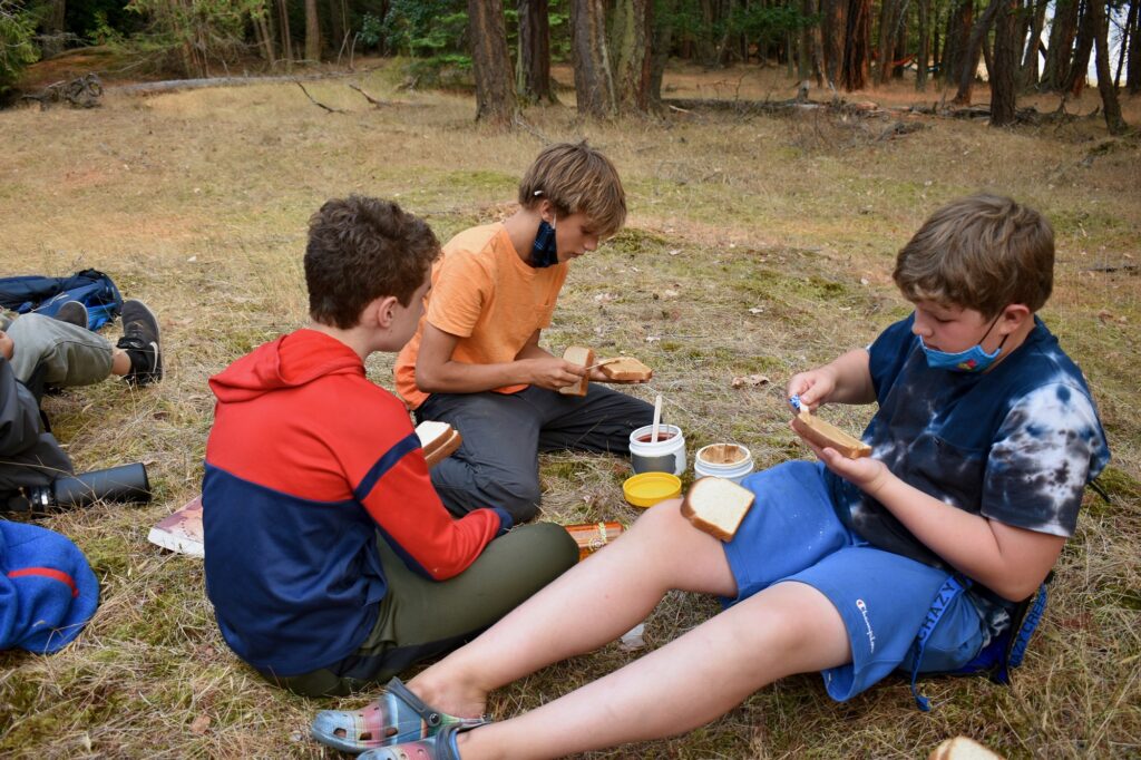 Three campers sit on the ground and make sandwiches