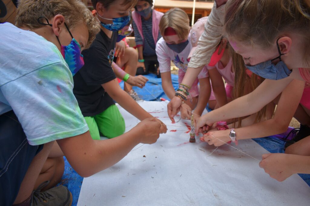 Campers wearing masks hold multiple strings connected to each other in the center of the photo