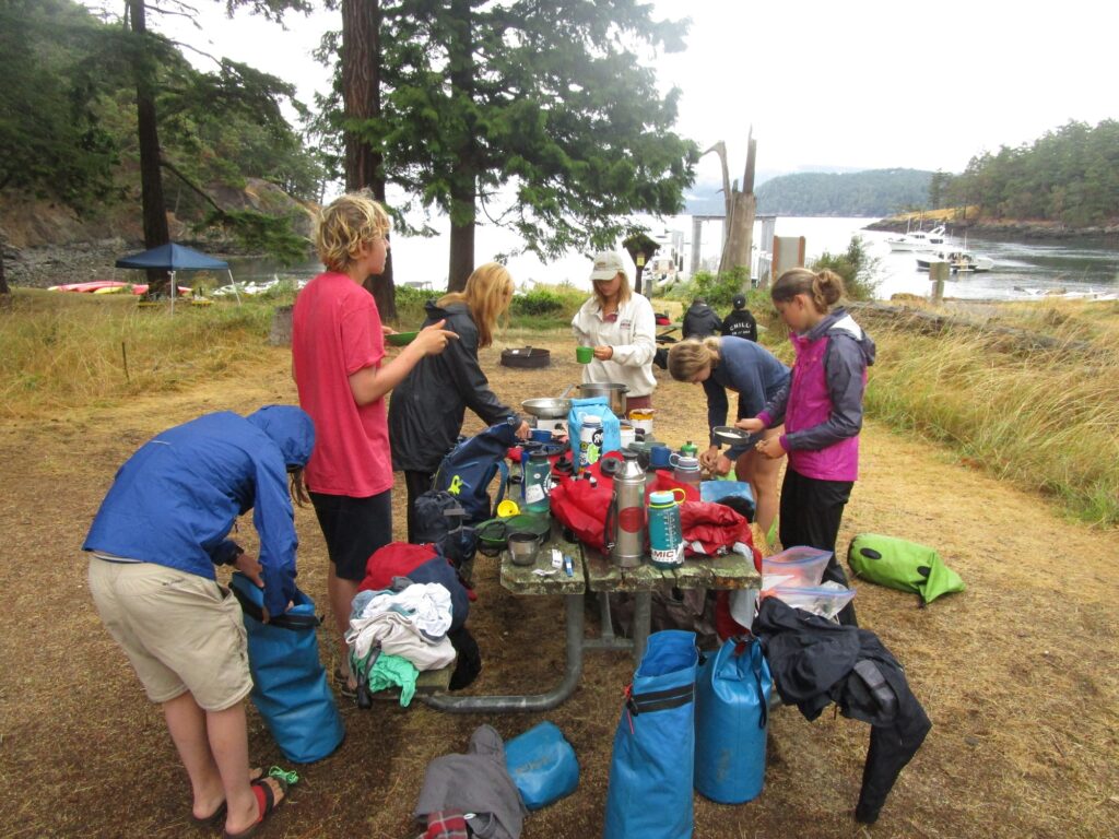 Campers gather around a picnic table covered with camping gear