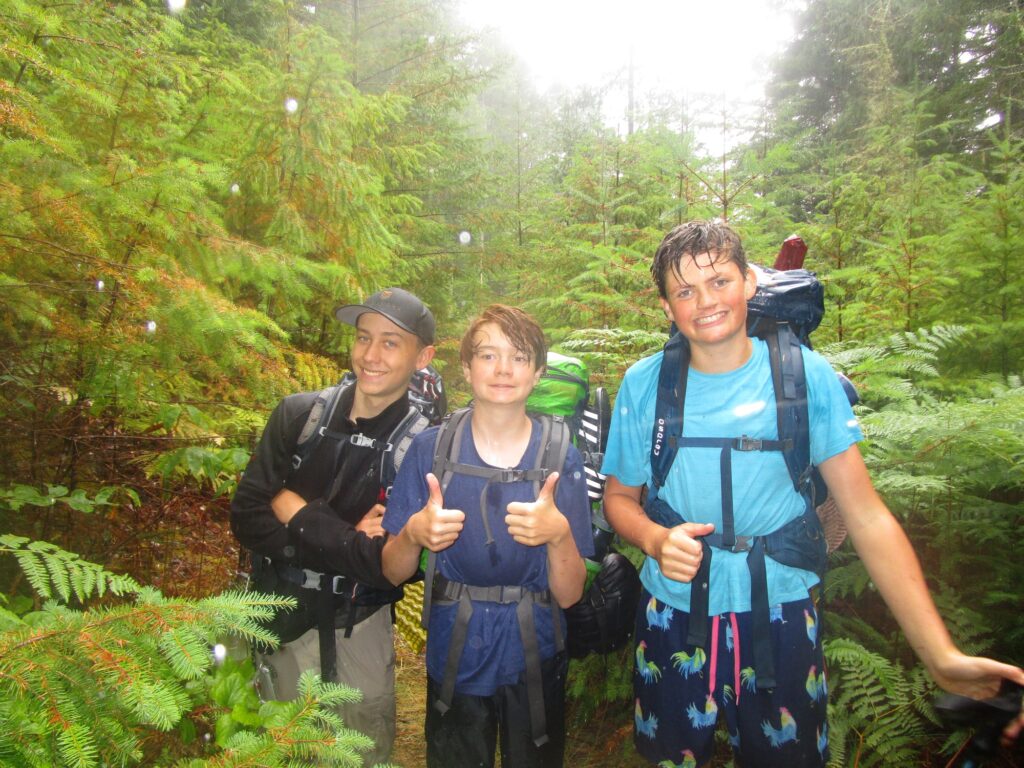 Three campers wearing backpacks smile and give the thumbs up sign